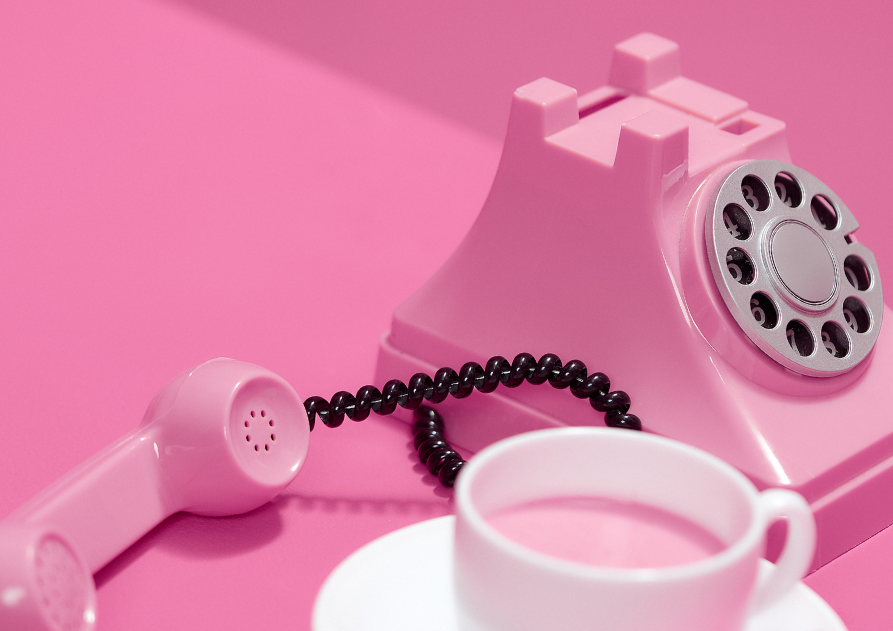 Teléfono antiguo y taza sobre fondo rosa