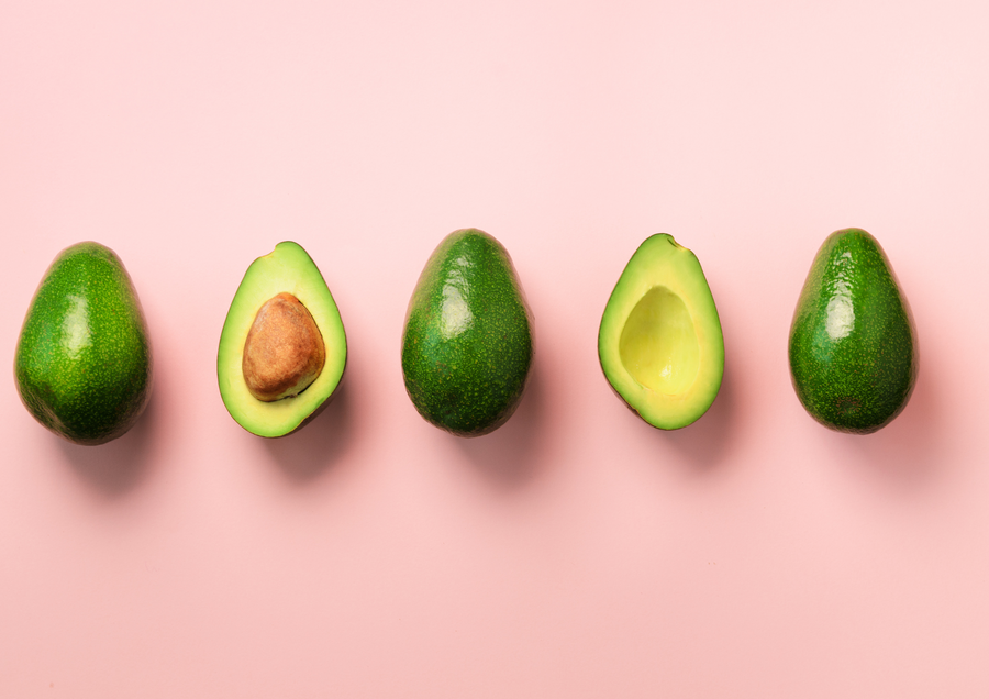 Aguacates enteros y partidos sobre fondo rosa