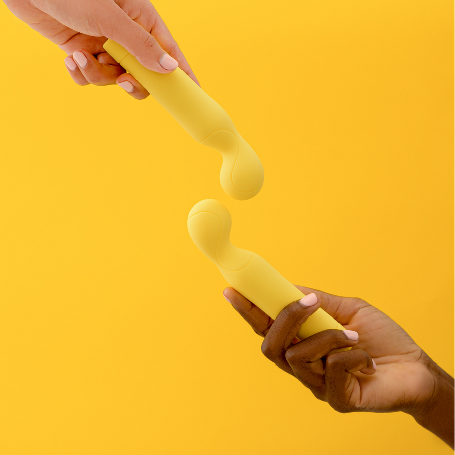Dos manos se pasan un vibrador amarillo sobre fondo amarillo
