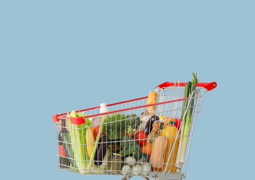 Un carro de la compra lleno de verduras, sobre fondo azul claro